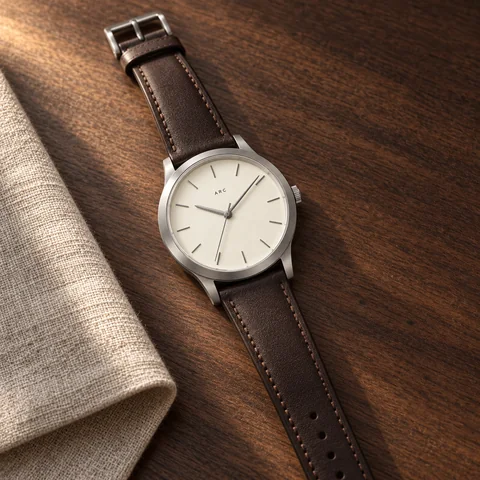 ARC watch on a walnut desk beside natural linen