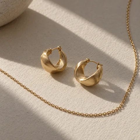 Brushed gold hoop earrings and a fine chain on textured paper